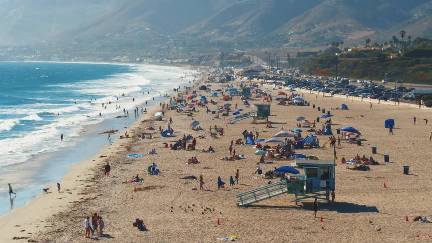 Aerial view of a large crowd of people on summer vacation on a beach near the mountains