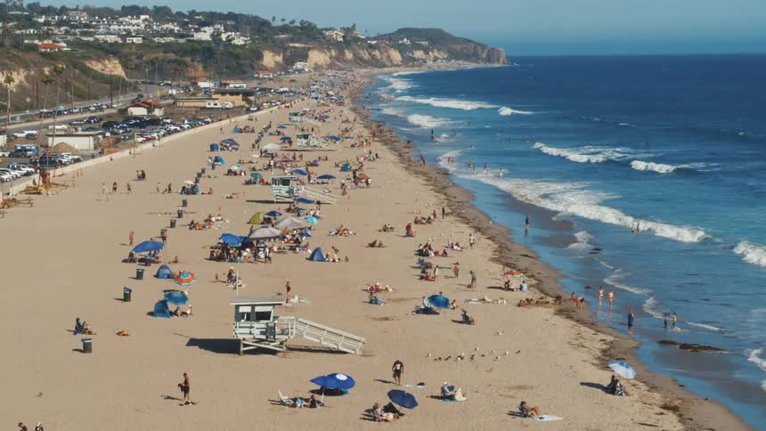 Aerial view of people lying down walking and swimming on the beach next to the wavy ocean
