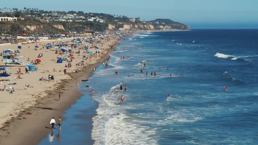 Crowds of people on summer vacation enjoy the beach and play in the surf