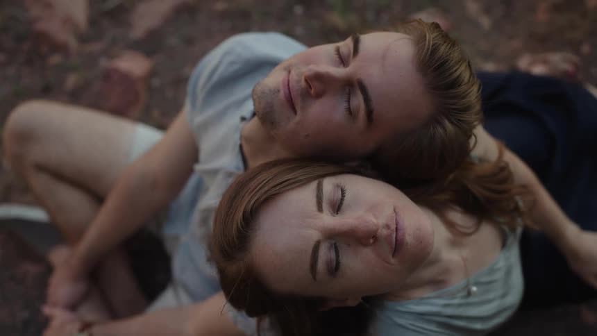 A man and woman are sitting in leaves with their heads back on each others shoulders