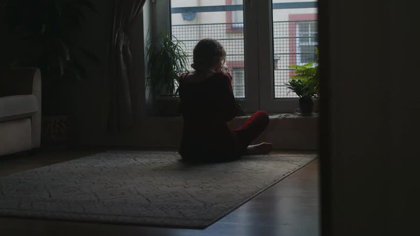 Young woman sitting on the floor in front of a window drinking a cup of coffee