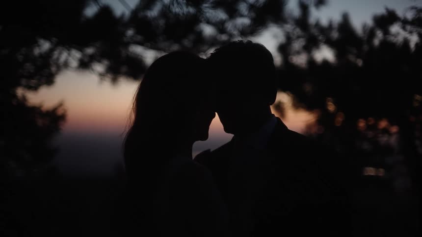 A man and woman holding each other close as the sun has set in the sky behind them