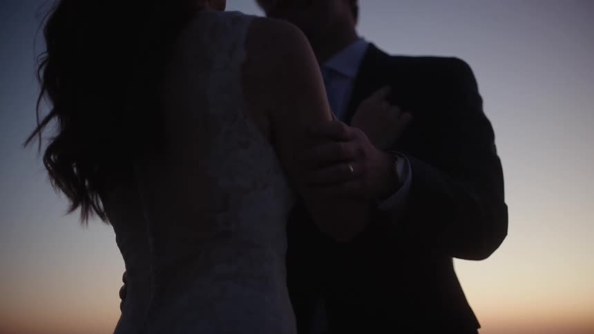 A man wearing a tuxedo strokes the arm of a woman wearing a wedding dress
