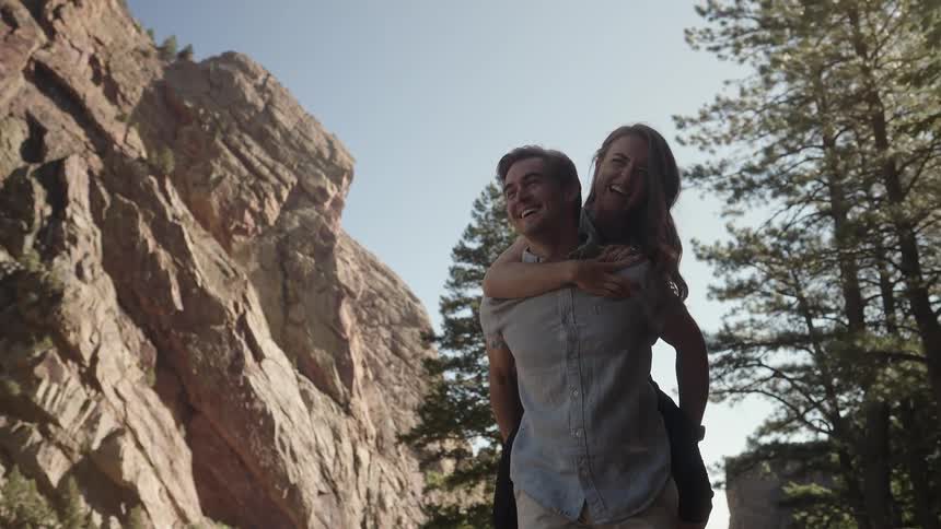 A man and woman laugh as he piggy backs her past a cliff
