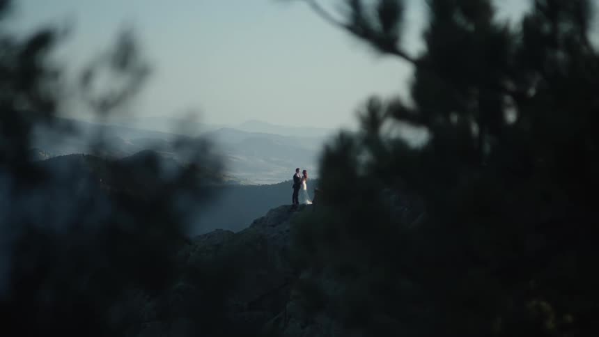 A man and woman standing on a mountain ridge getting married in gown and tuxedo