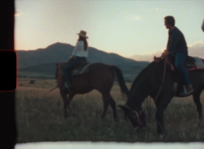 Woman with hat and white shirt sits on horse next to men on horseback in the field at sunset in super 8 film