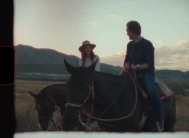 A man and woman laugh while riding horses on a ranch in super 8 film
