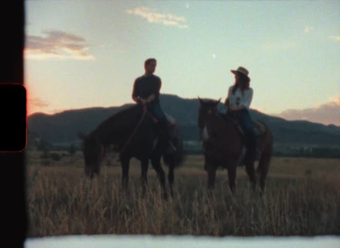 Young couple leisurely riding horses on the plains next to the mountains at evening caught on vintage film