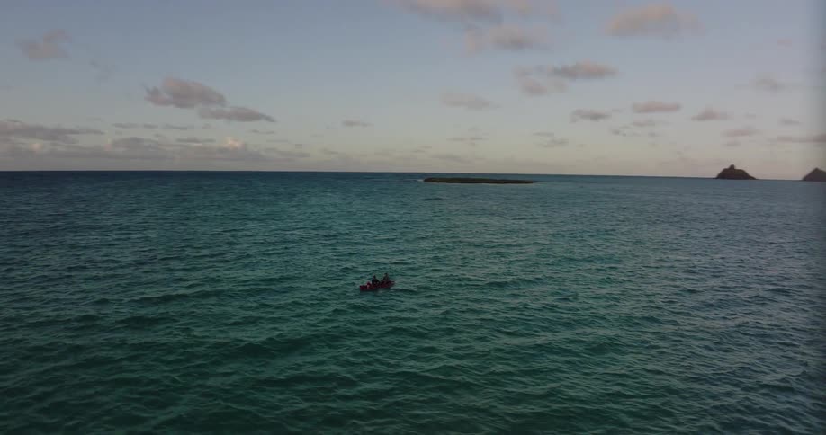 In a vast ocean two people in a canoe are right in the middle of it and look tiny while the camera orbits around them