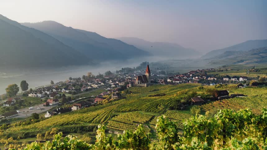 Time lapse of a vineyard close to a small town covered in mist next to a river in the mountains