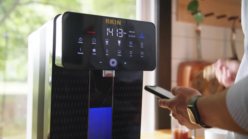 A man eating a bowl of food next to a coffeemaker while holding his phone
