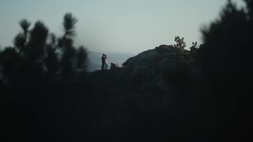 Formally dressed couple hug each other near the top of a mountain at morning