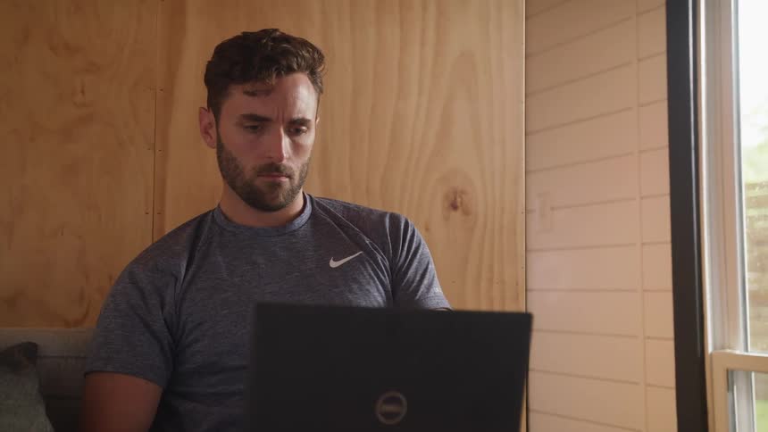 A man typing on a laptop while sitting on an indoor chair
