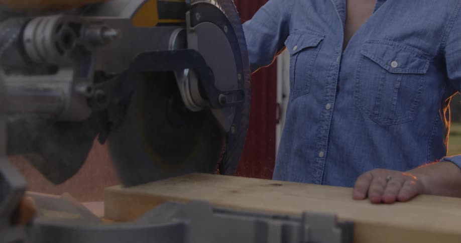A woman is using a saw on a piece of lumber