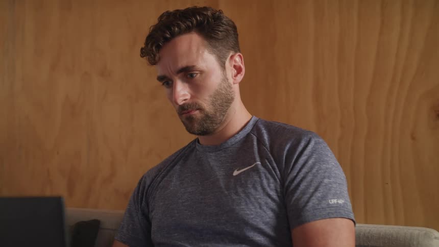 A man uses a laptop on his lap while sitting on a sofa indoors