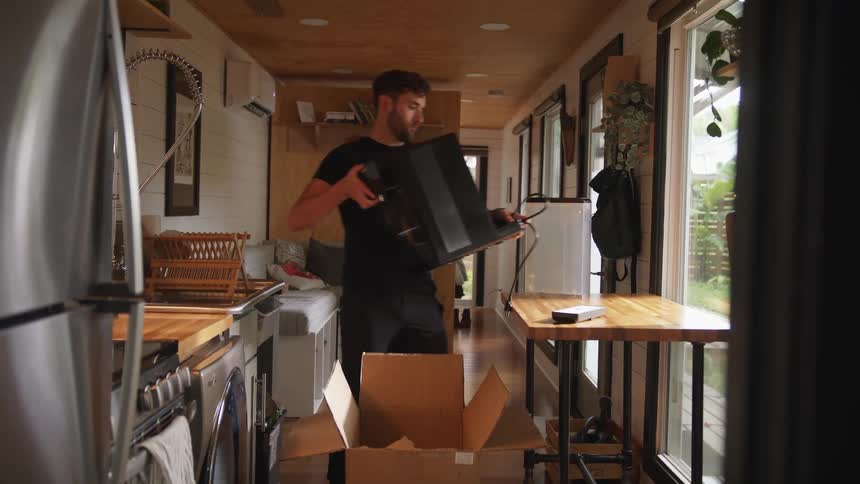 Man with beard black shirt and pants puts new espresso machine on table in the kitchen