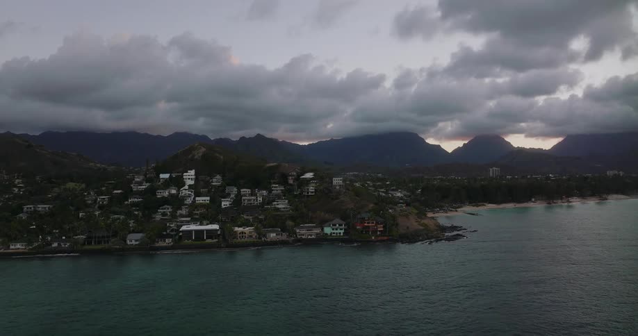 Aerial view of a small coastal town next to the ocean while the sun sets behind the mountains