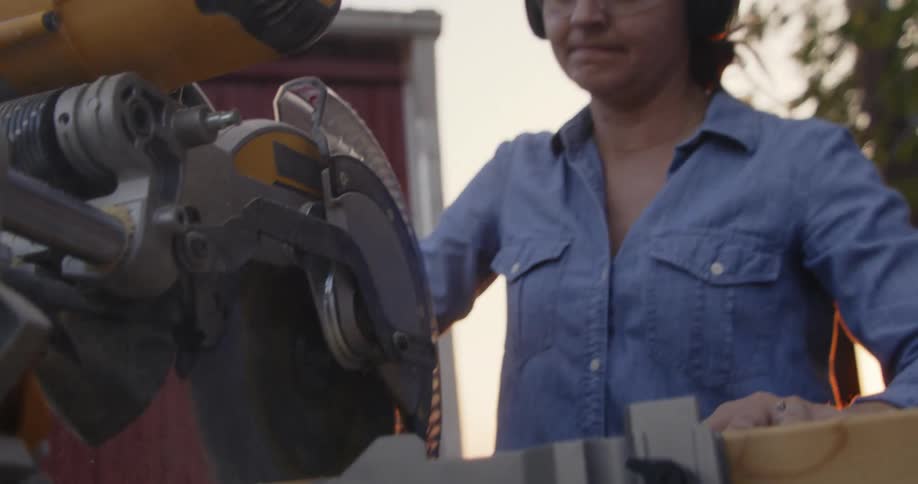 A woman cutting a piece of wood outside with a power saw