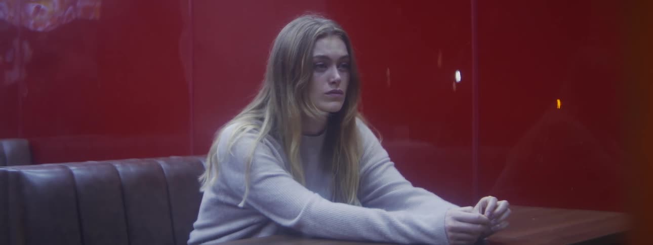 Young blonde woman wearing a white sweater sitting on a table at a restaurant looks out the window