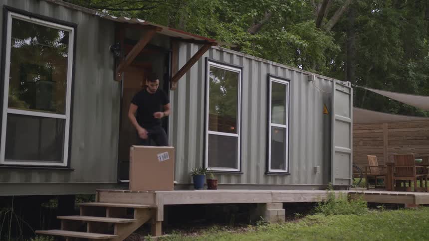 A man steps outside to retrieve a package from his front porch