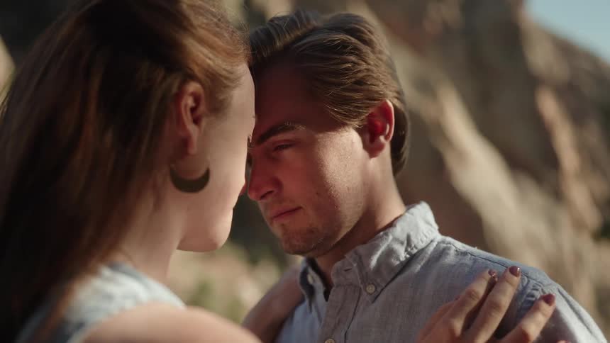 Woman with brown hair earrings and blouse and man with blue shirt look into each others eyes in the mountainous area
