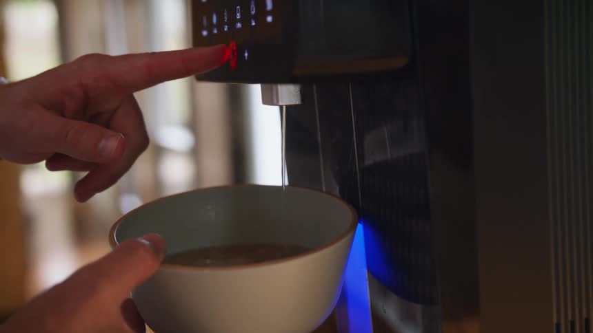 A person is holding a cup under a coffee machine and they push a button to turn it off