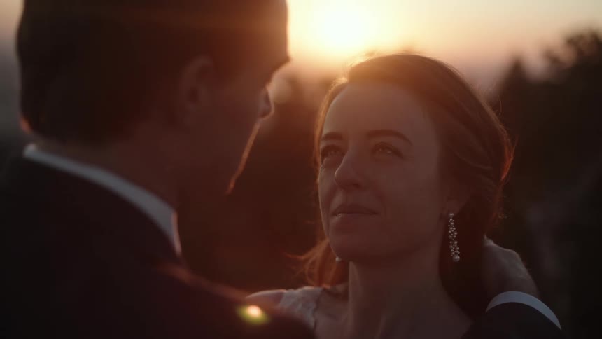 Man wearing a tuxedo lovingly touches the hair of a woman outdoors at sunset