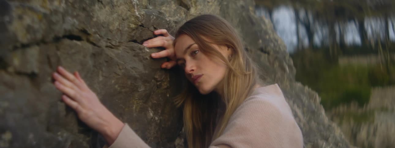 Woman leans her body against a rock wall while stroking the rocky surface
