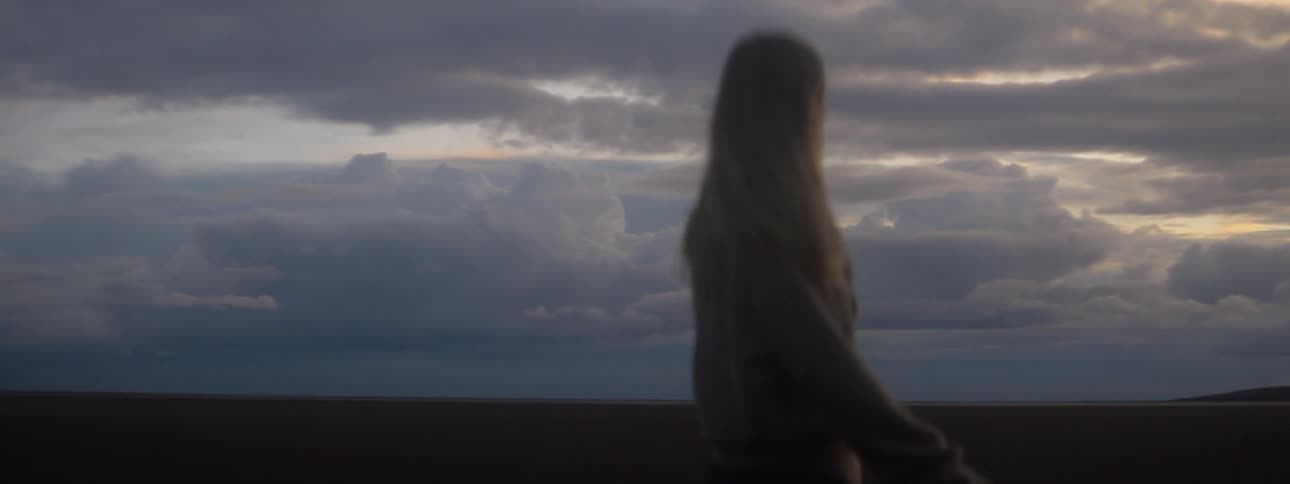Woman wearing sweater walks through hilly terrain under an overcast sky