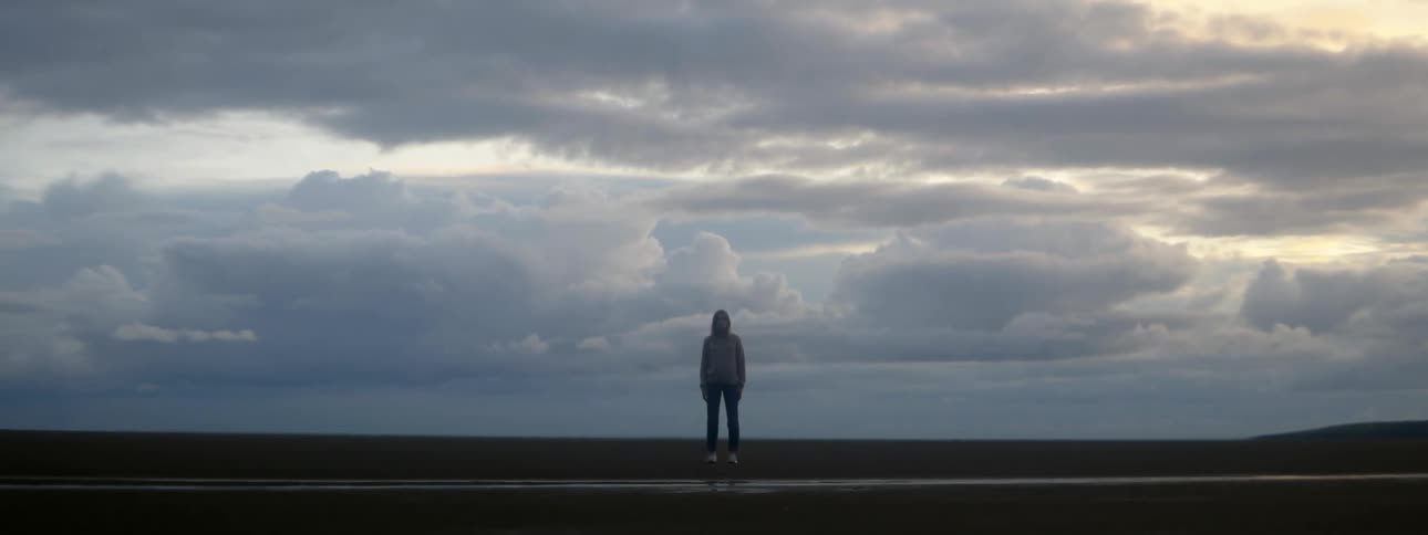 Woman stands on river bank on misty day under an overcast sky
