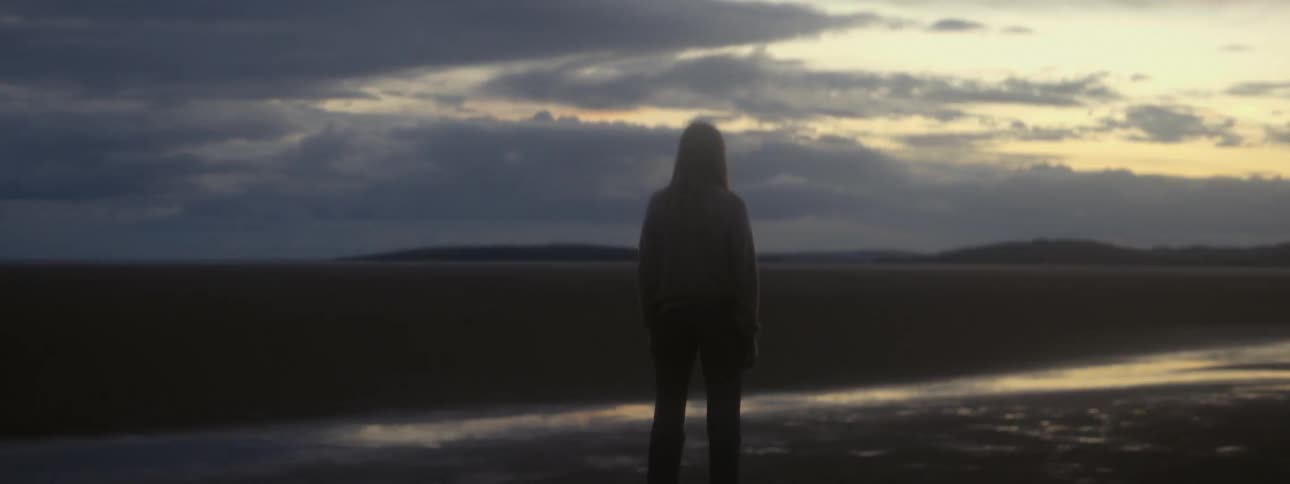 The silhouette of a woman can be seen as she stands beneath a cloudy sky