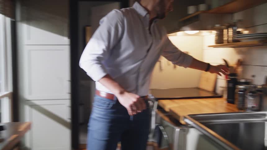 Man with beard blue shirt and jeans walks in kitchen to use espresso machine