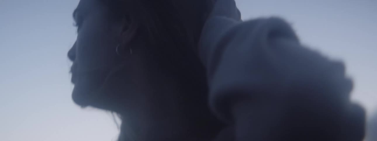 A woman is walking outside and she runs her hand over her hair as she turns her head