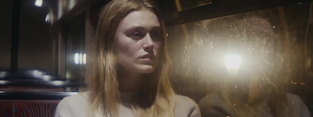 A sadlooking woman sits on a moving bus at night and stares out the window