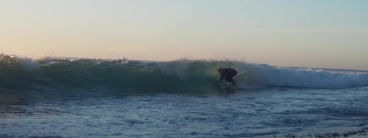 Long haired surfer rides a surfboard on a small wave near the coast at evening
