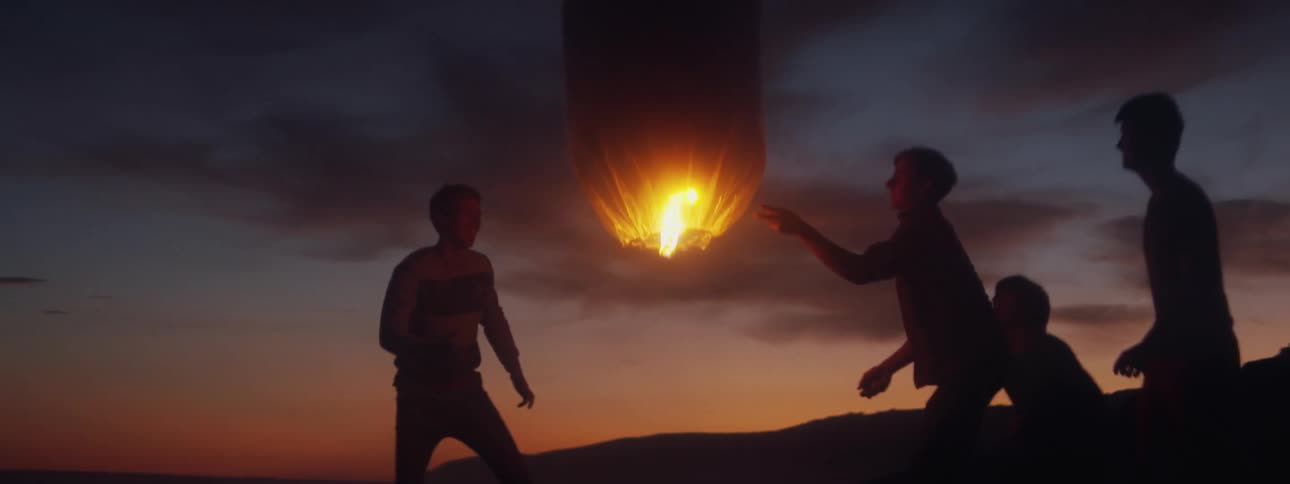A group of young men light a lantern balloon and watch it fly away