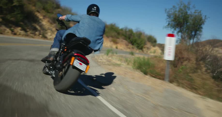 Biker wearing black helmet blue shirt and jeans rides motorcycle on mountain highway