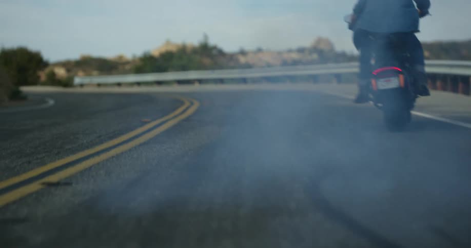 A man starts up his motorcycle and rides down a curved highway