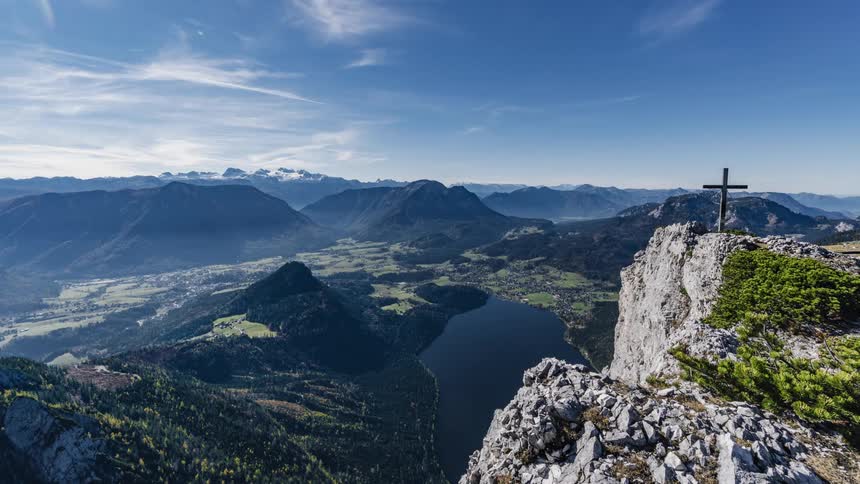 Panoramic view of a cross atop a mountain next to a lake on a valley