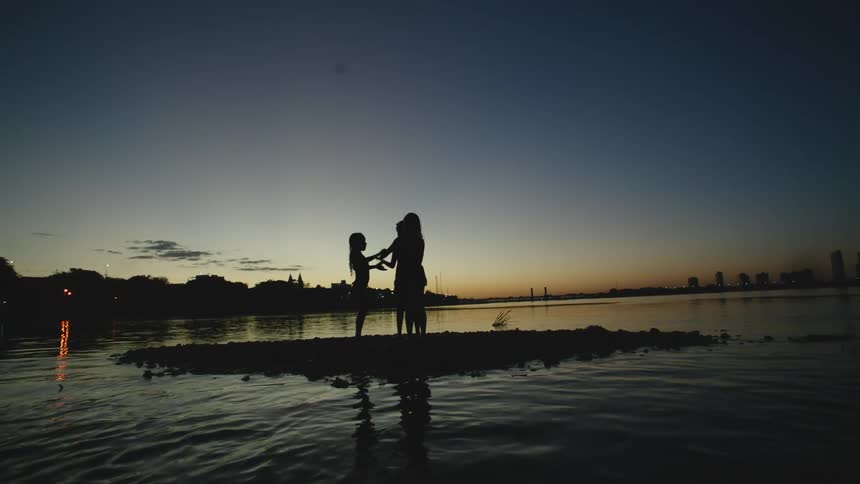 A group of girls play a clapping game together on a tiny island in a waterway at sunset