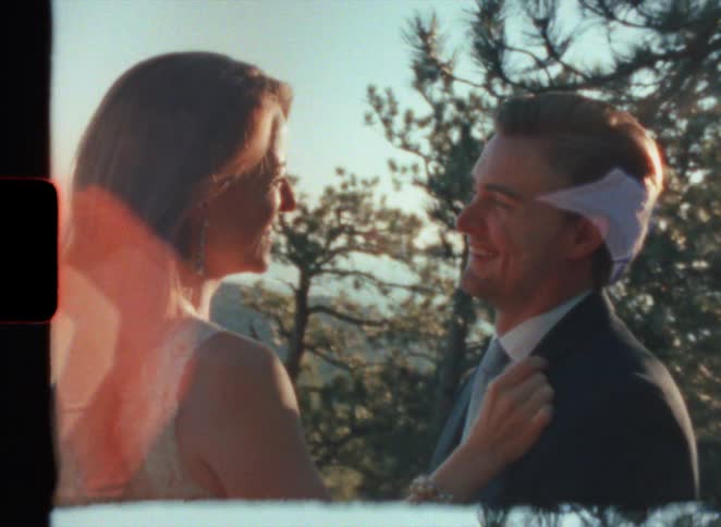 Sunlight shines behind a formally dressed couple looking at other near the top of a mountain at evening in super 8
