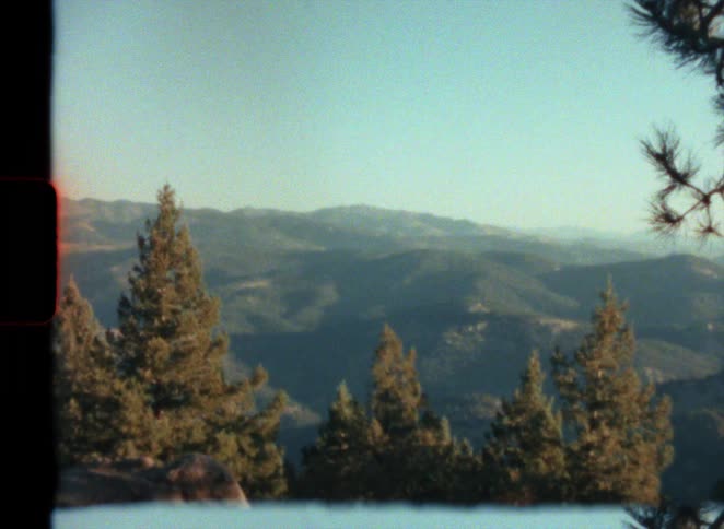A mountain range is covered in a forest of pine trees caught on vintage super 8 film