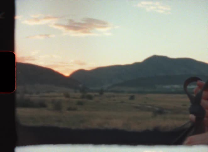 Young couple leisurely riding horses on the plains next to the mountains at evening in super 8 film