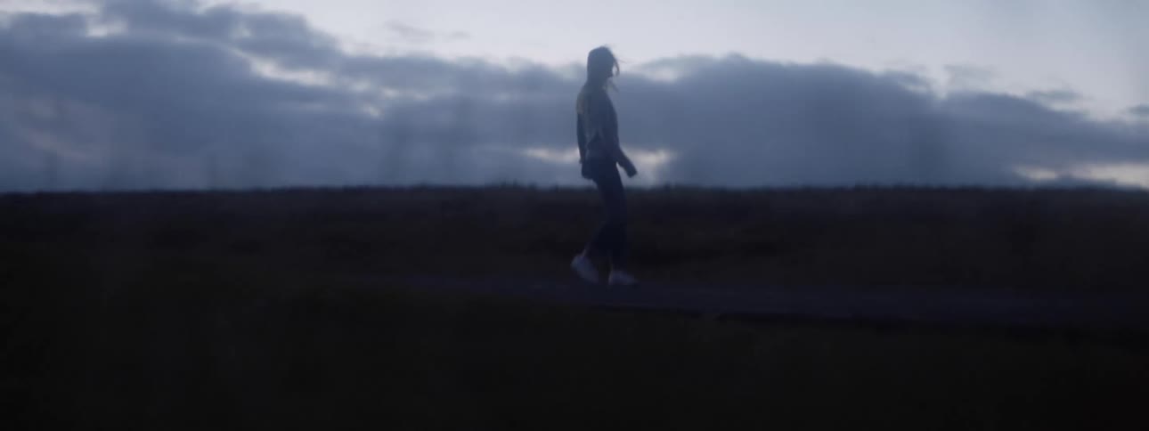 Young woman wearing a hoodie walking on a path on a field at evening