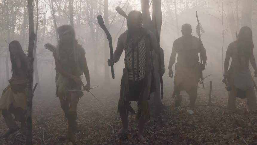 Tribal people walking cautiously through a smoky forest at sunset