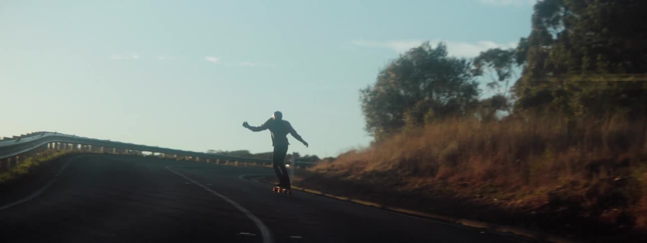 Male skateboarder wearing helmet shirt and pants skateboards down mountain highway