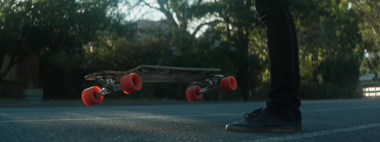 Skateboard falling and bouncing on the ground next to a standing person