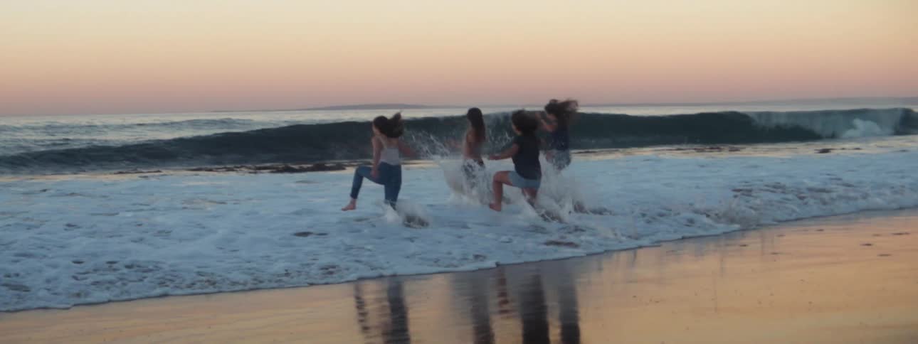 A group of friends run into the ocean in unison