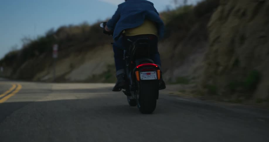 A man wearing denim apparel starts driving his motorcycle along a curved road
