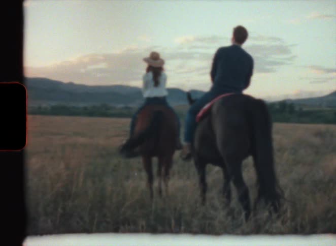A man and woman ride horses through a field caught on vintage super 8 film